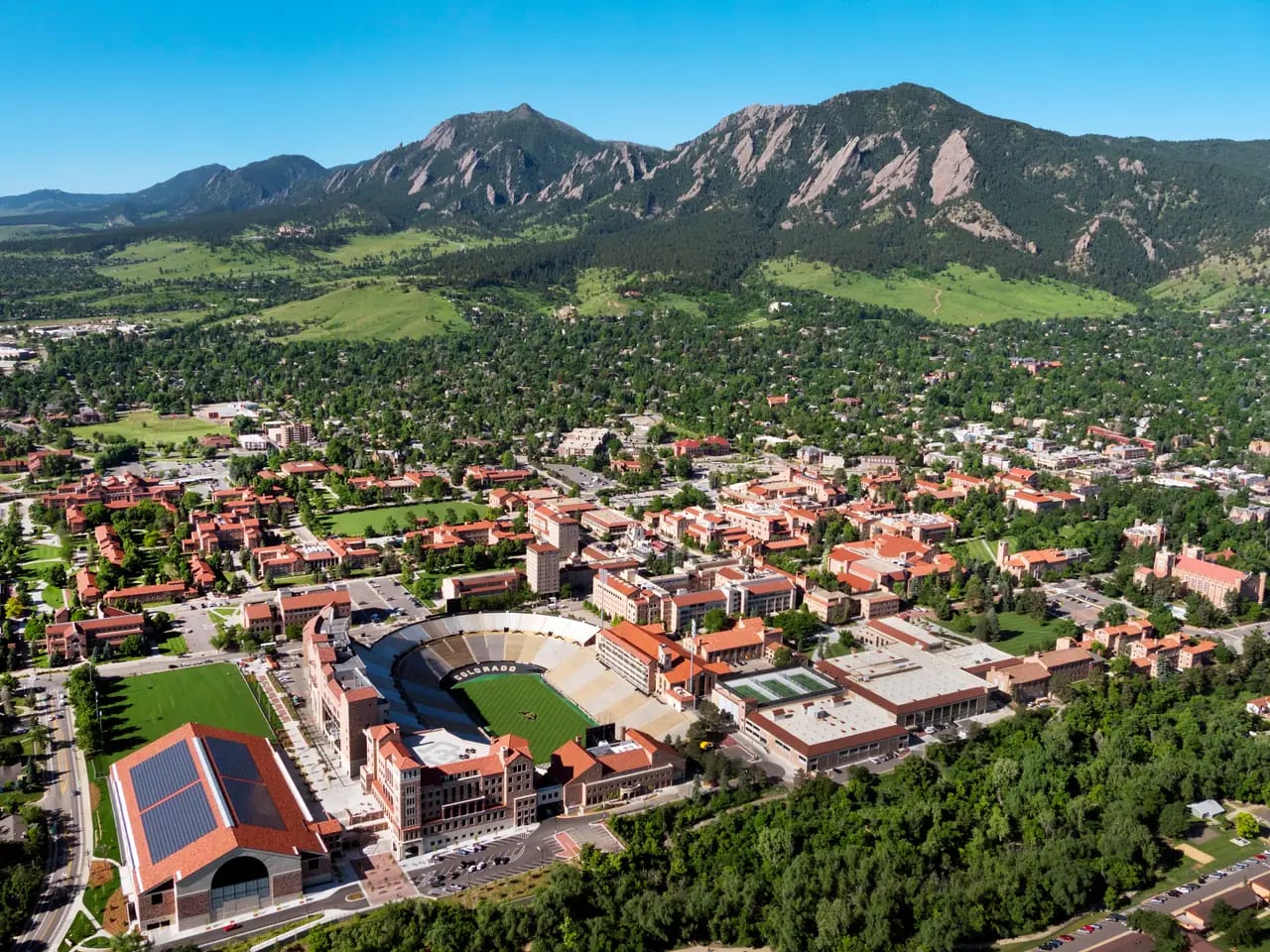 An aerial view of a university campus and stadium beneath the mountains