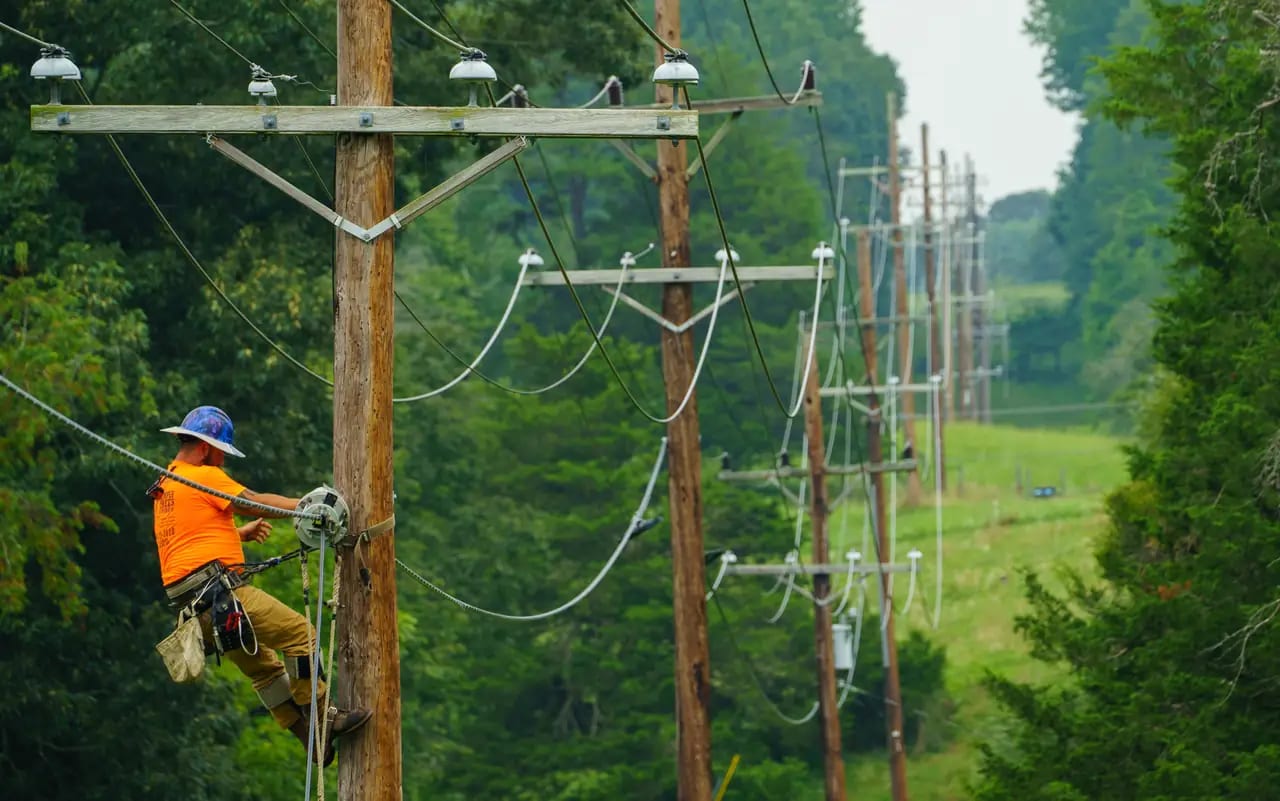 A lineworker maintaining a utility pole beside a rural road