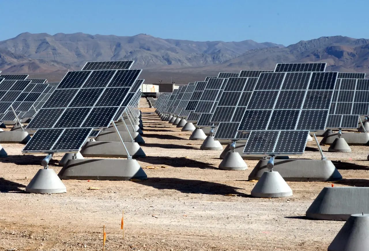 Rows of solar panels at a military installation with desert mountains beyond