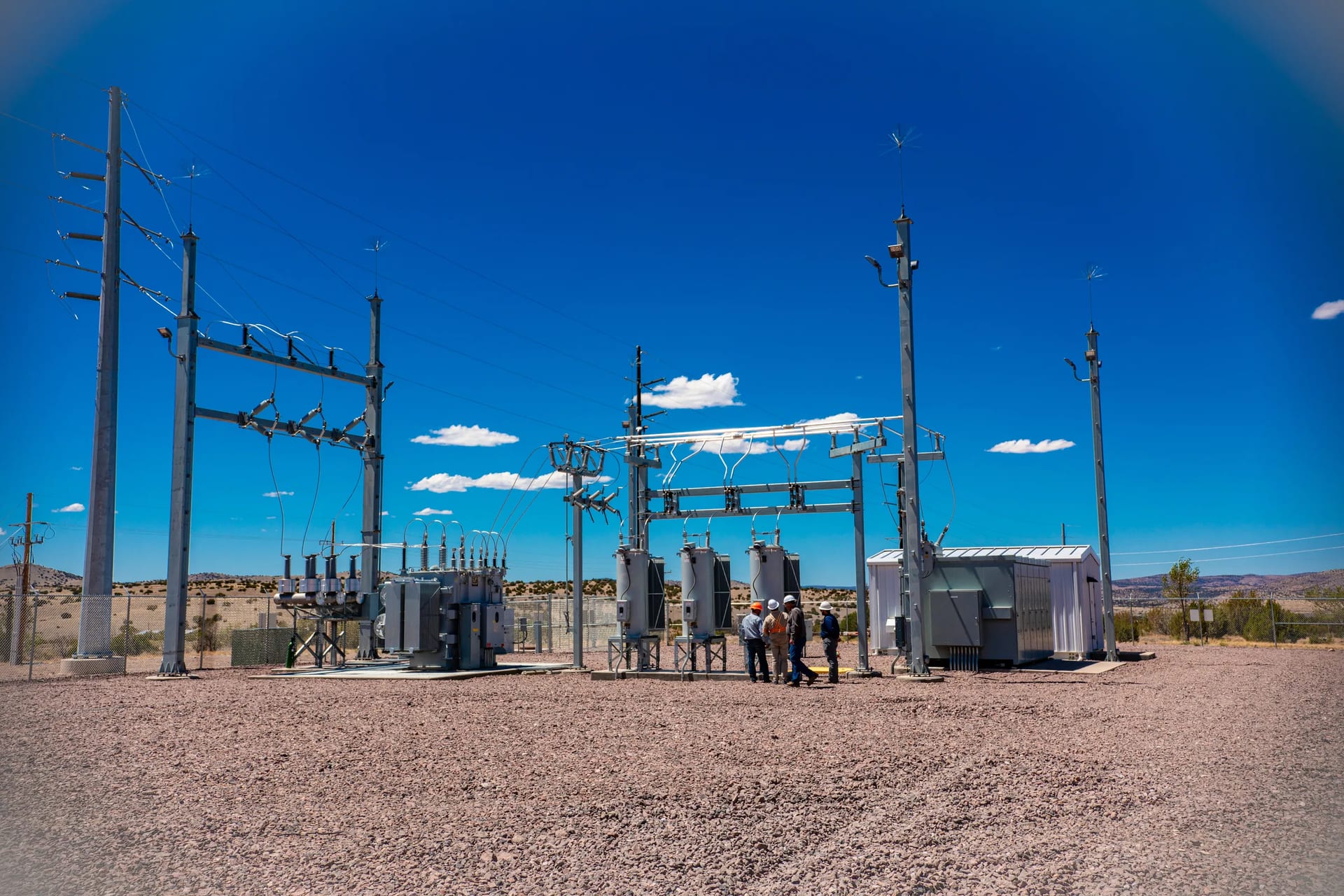 Electrical equipment and a field crew at a substation beneath a blue sky.