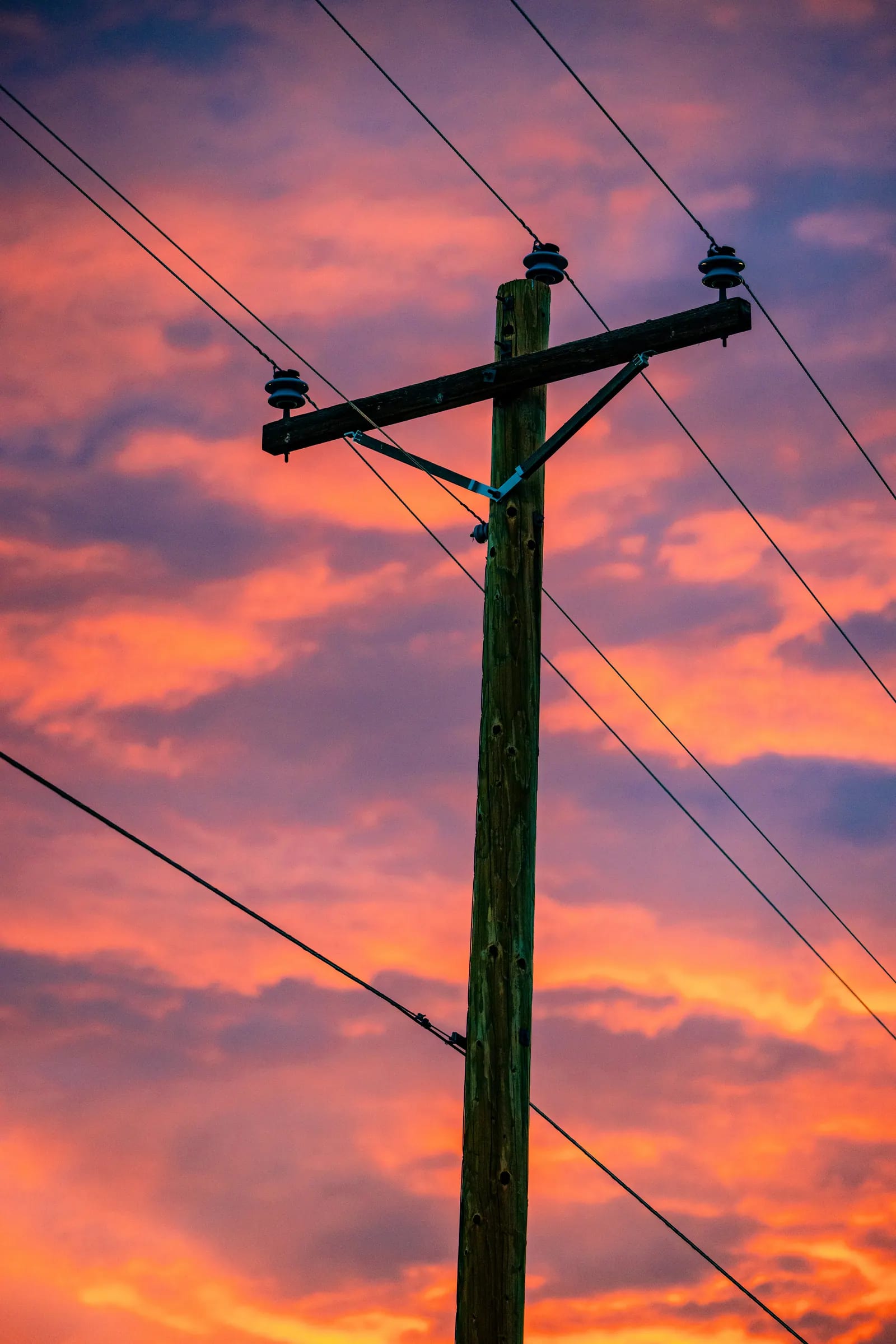A utility pole and power lines silhouetted against a pink and orange sunset