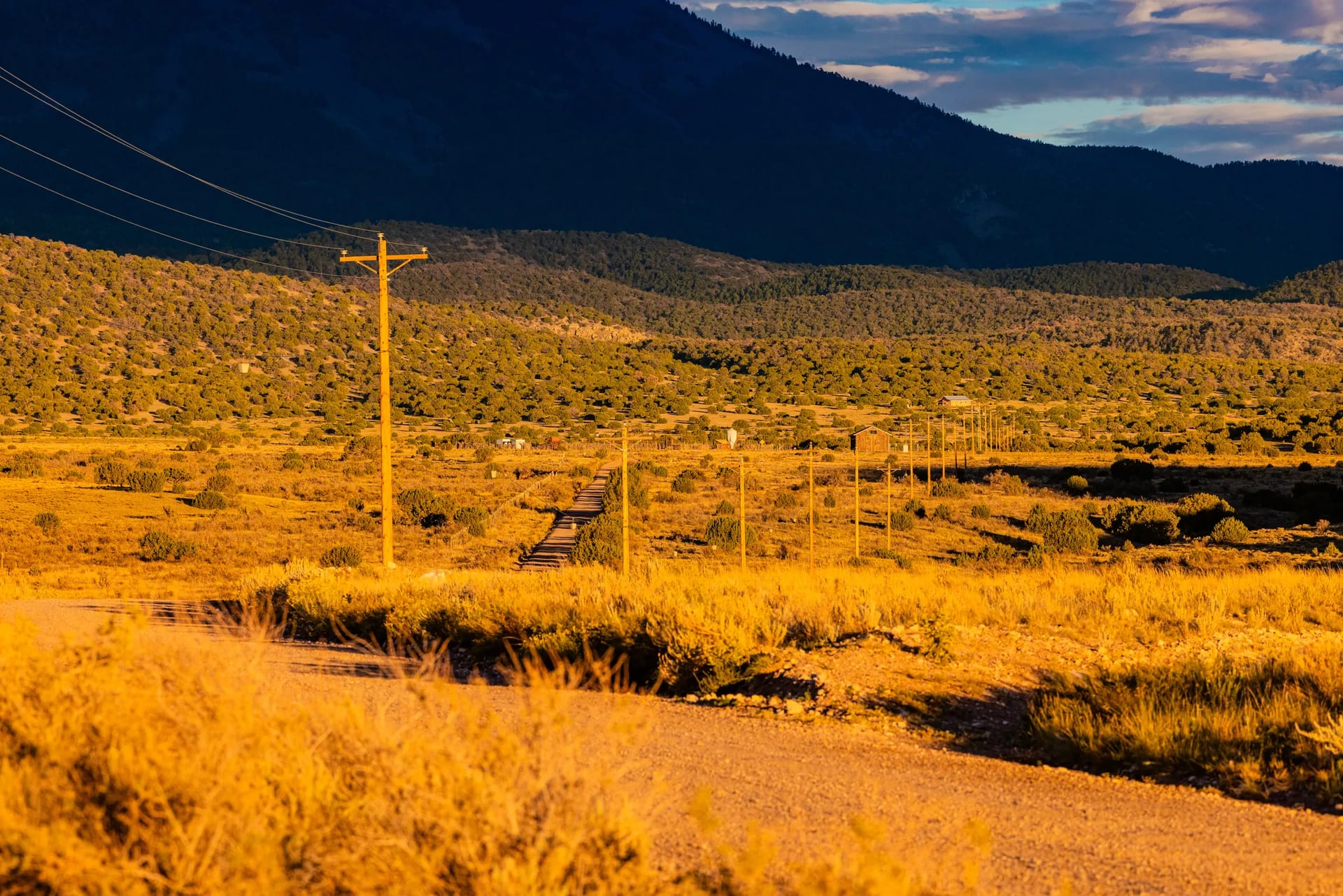 Power lines following a dirt road through golden high-desert vegetation and mountains near Socorro